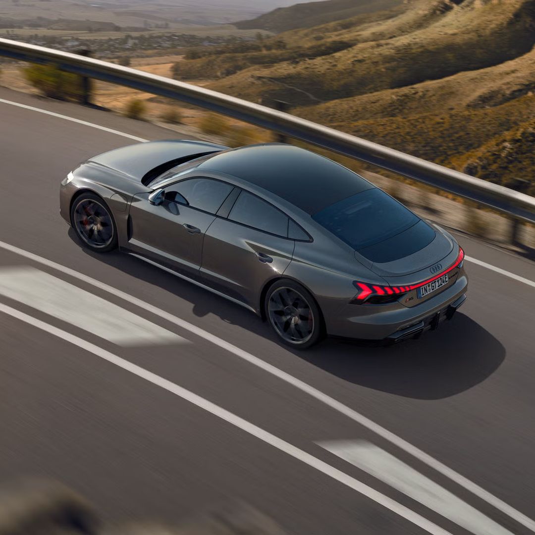 Ein grauer Audi RS e-tron GT fährt auf einer kurvigen Bergstraße mit leuchtenden Rücklichtern.