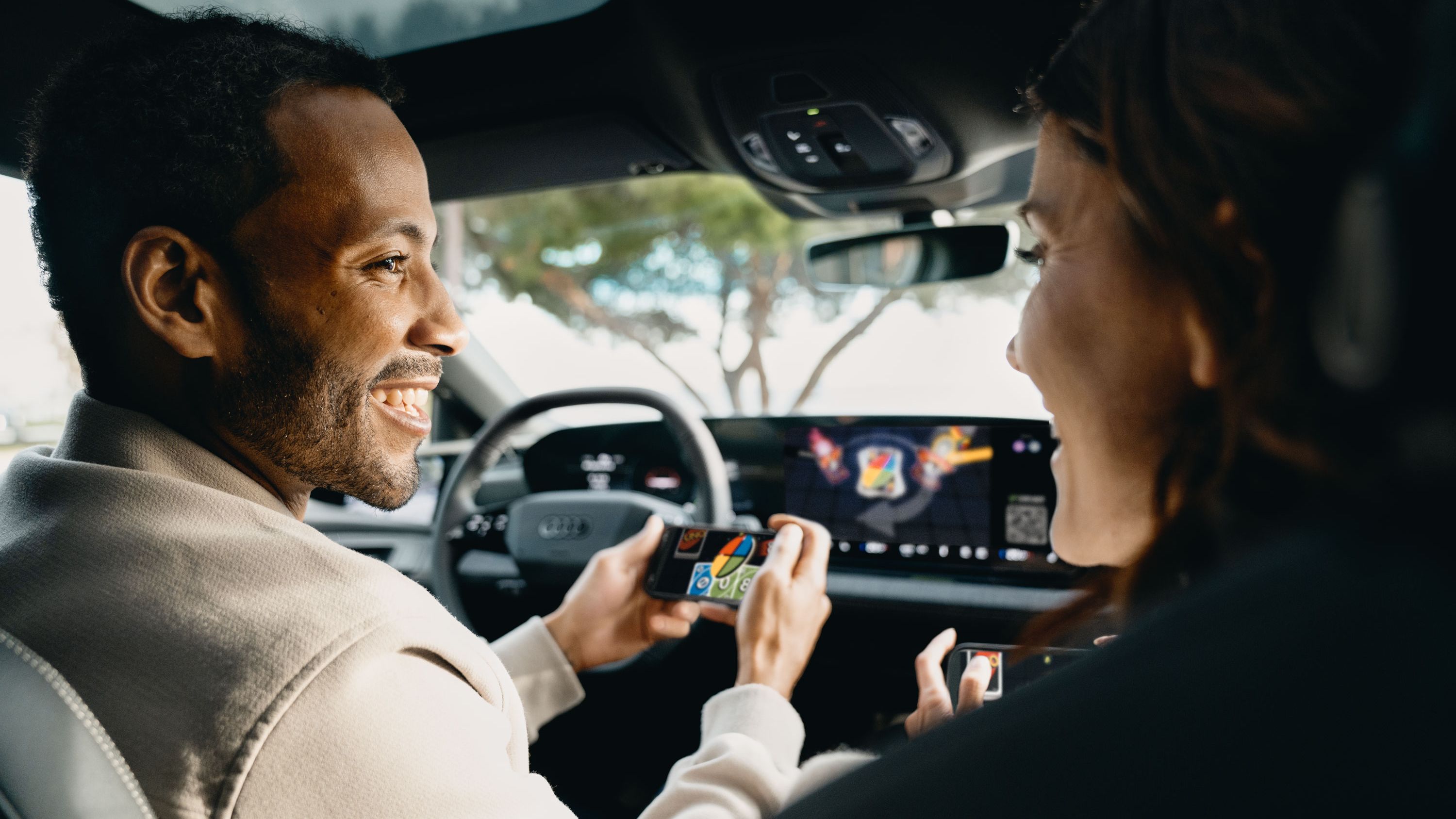 Zwei Personen sitzen in einem Audi, die vordere Person hält ein Smartphone in der Hand. Die Personen sind in ein Spiel auf dem Smartphone vertieft.