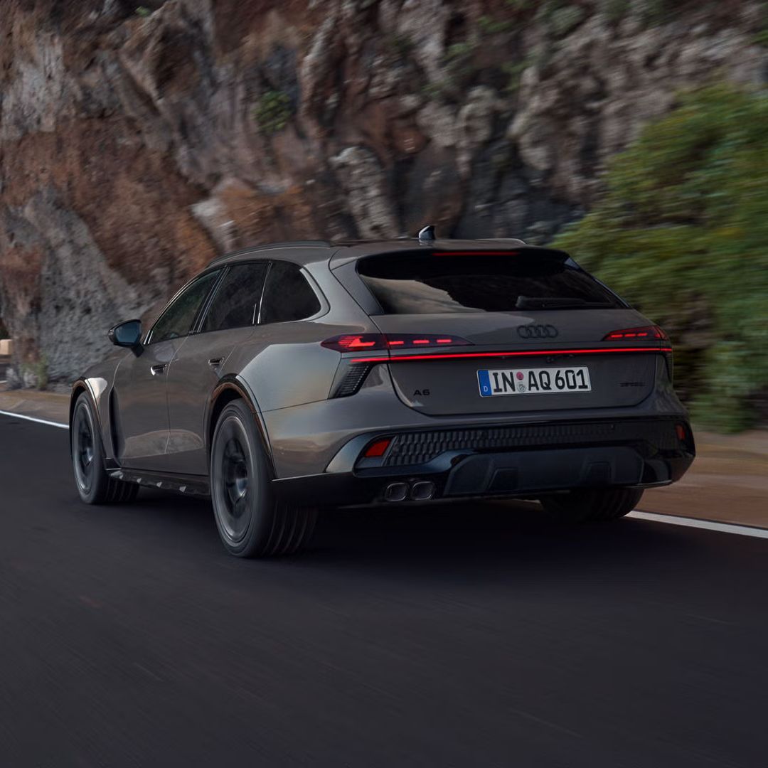 Der Audi A6 allroad schräg von hinten in voller Fahrt auf einer Gebirgsstraße. Rechts ragen steile Felswände auf.
