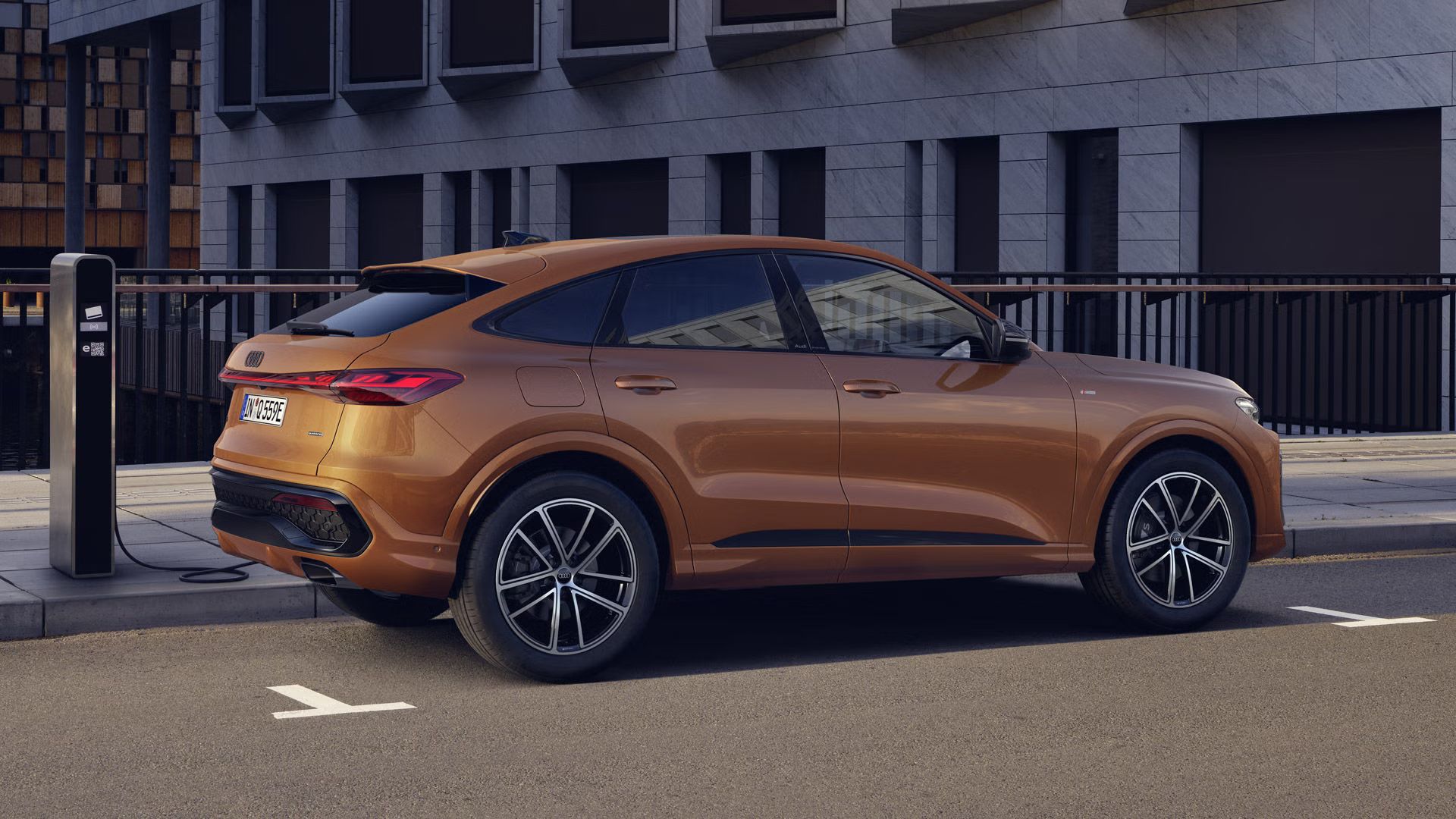 Der Q5 Sportback mit der Individuallackierung Ipanembraun Metallic steht auf einer Brücke und ist an eine Ladestation angeschlossen.