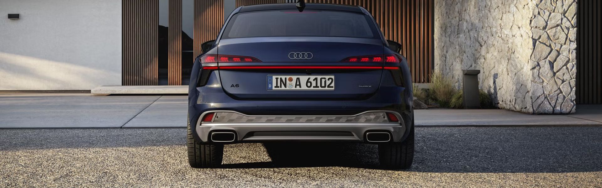 Die A6 Limousine in der Heckperspektive. Das Fahrzeug steht einem modernen Haus zugewandt.