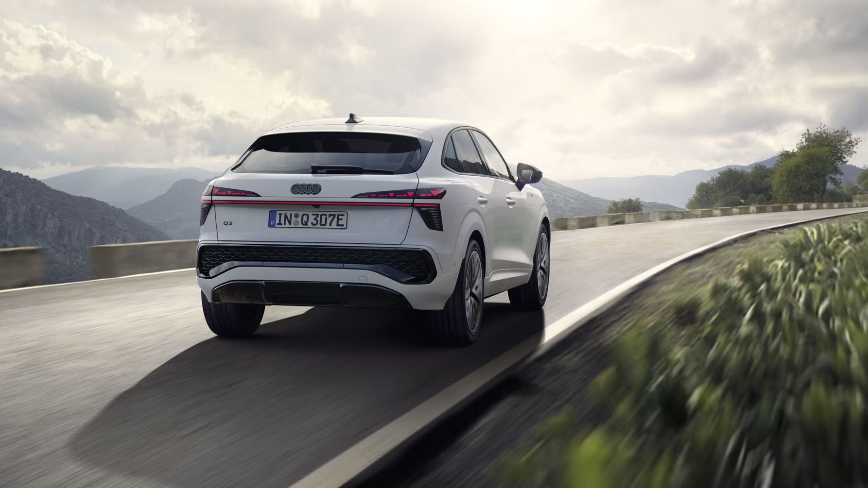 Ein weißer Q3 Sportback e-hybrid fährt auf einer Landstraße in einer bergigen Landschaft.	