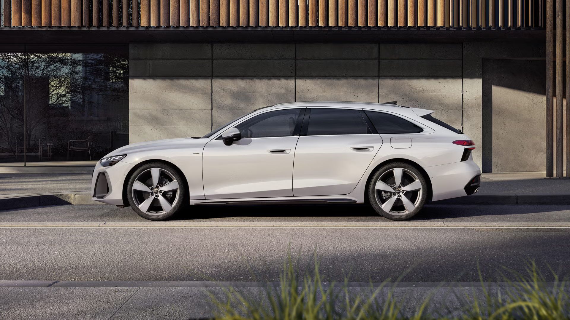 Der A6 Avant e-hybrid steht im Seitenprofil in einer Parkbucht vor der Fassade eines Gebäudes.