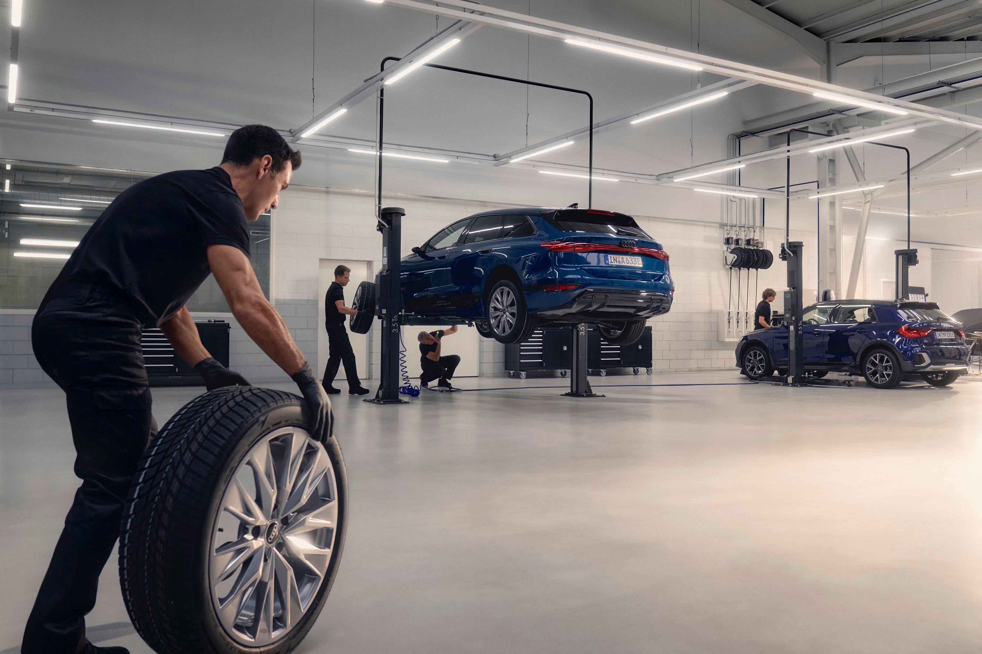 Ein Audi Mechaniker rollt ein Winterkomplettrad in Richtung eines Audi auf einer Hebebühne.
