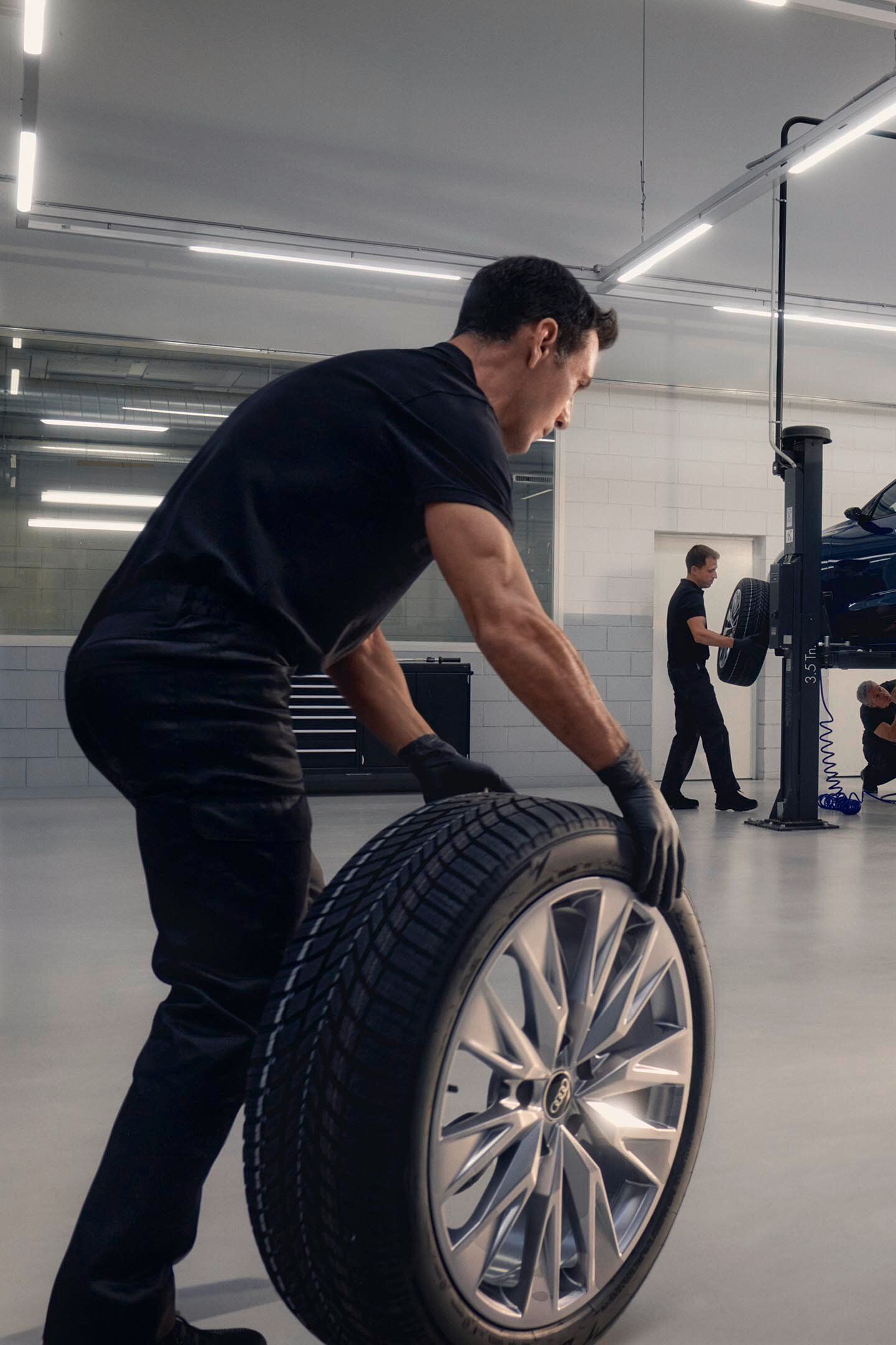 Ein Audi Mechaniker rollt ein Winterkomplettrad in Richtung eines Audi auf einer Hebebühne.