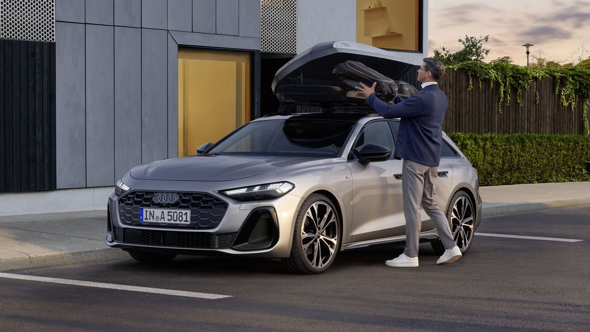 Der A5 Avant steht seitlich geparkt vor einem großen Gebäude. Ein Mann steht neben dem Fahrzeug und lädt Gepäck in die geöffnete Dachbox.