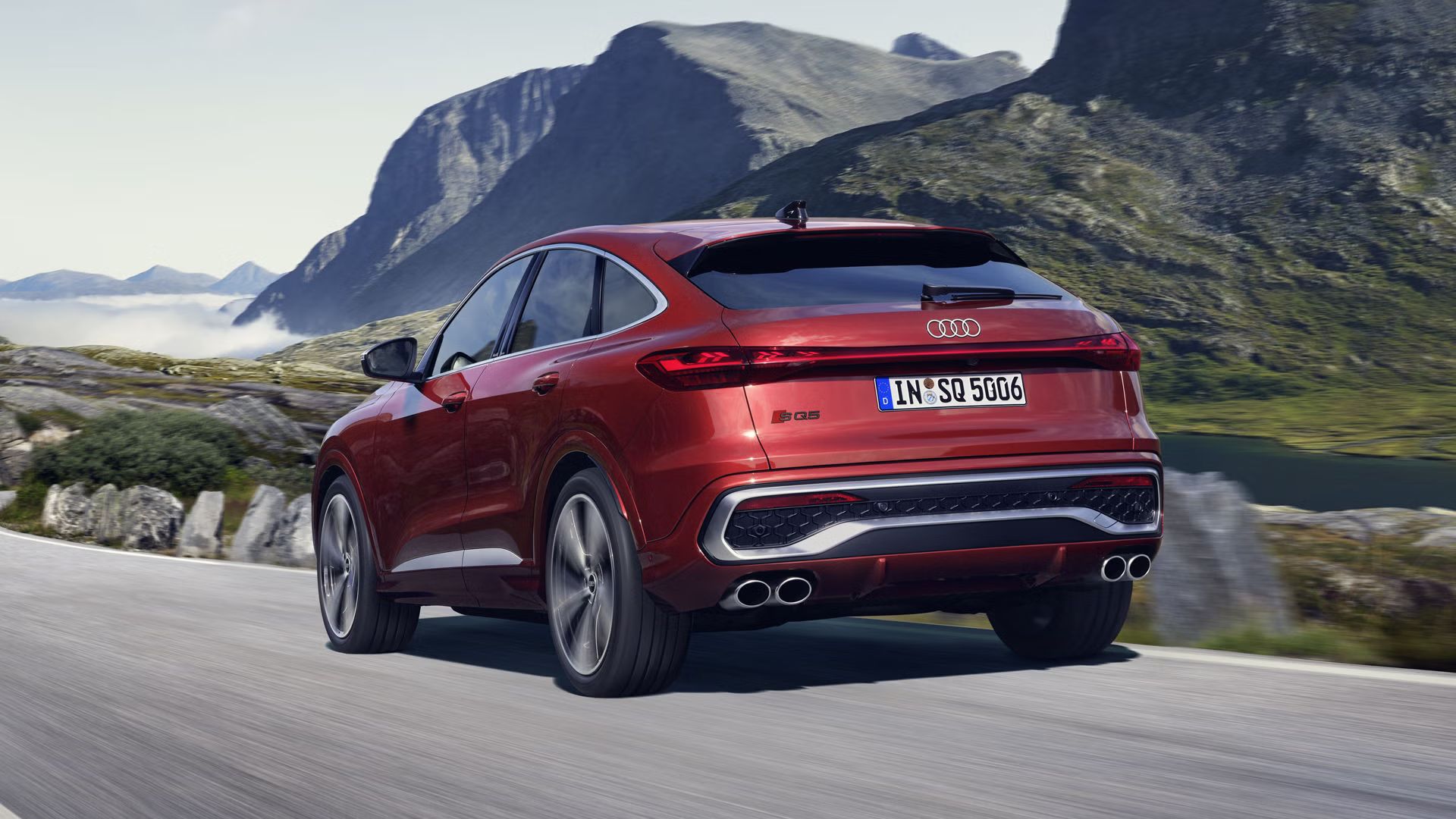 Schräges, hinteres Seitenprofil des roten SQ5 Sportback, welcher auf einer Straße durch die Berge fährt.