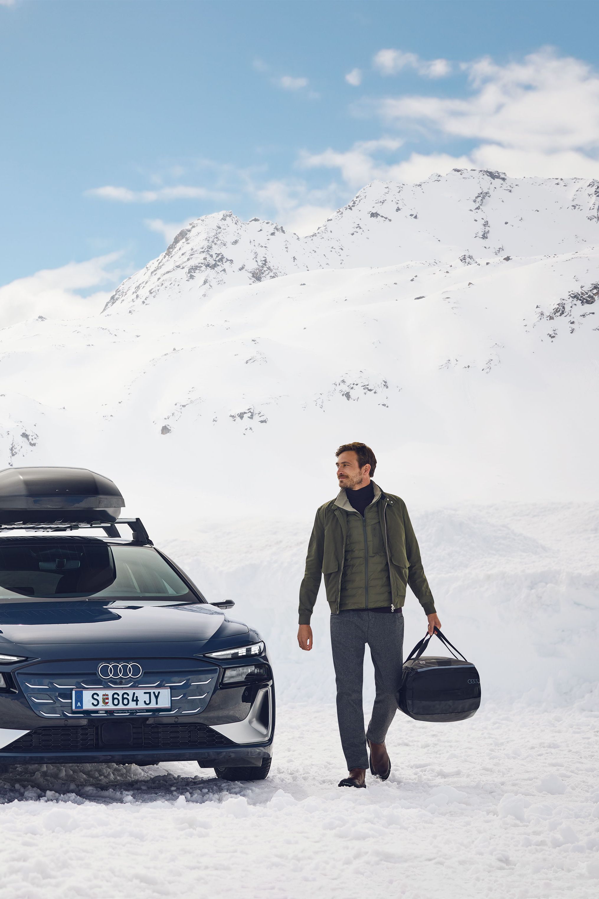 Ein Audi S6 mit Dachbox parkt in den winterlichen Bergen. Ein Mann und eine Frau verlassen das Fahrzeug.