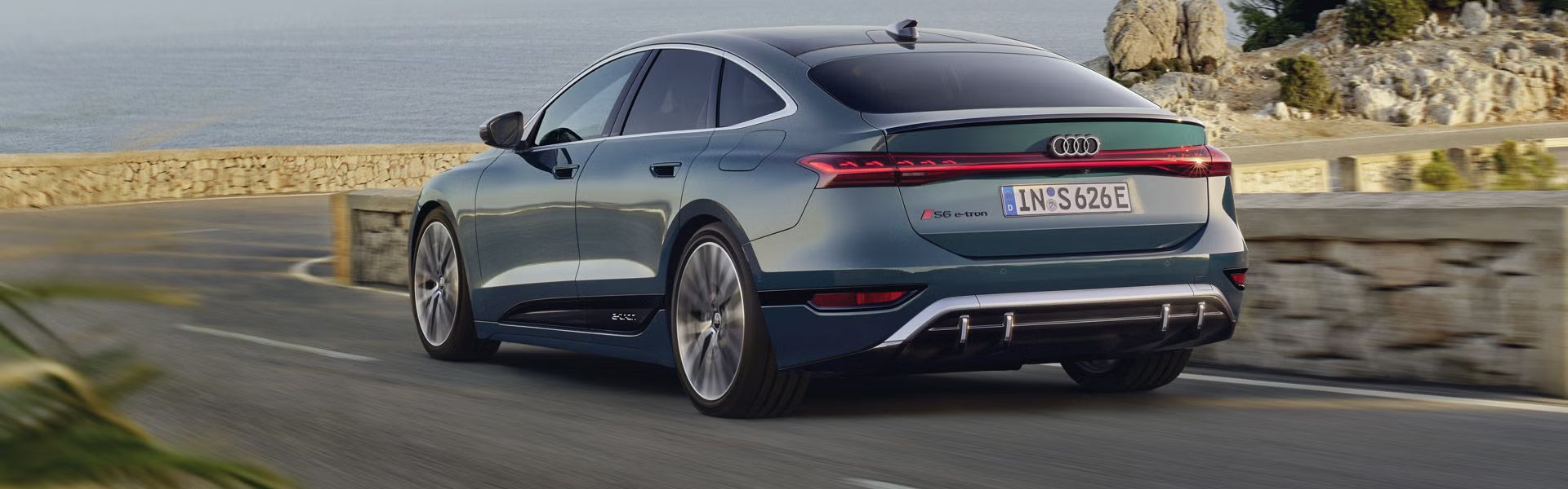 Der S6 Sportback e-tron im schrägen Heckprofil, während er eine kurvige Küstenstraße entlangfährt.