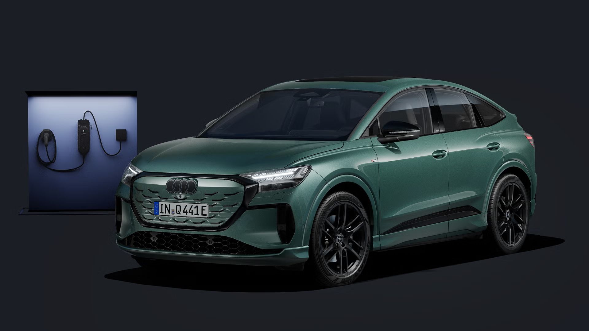 Der Q4 Sportback e-tron schräg von vorn auf dunklem Hintergrund, dahinter eine moderne Ladesäule.