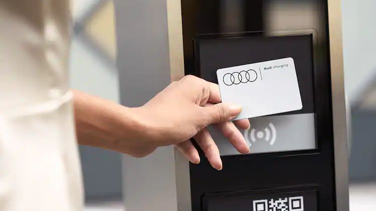 Eine Frau hält eine Audi charging card an eine E-Ladesäule zum Bezahlen.