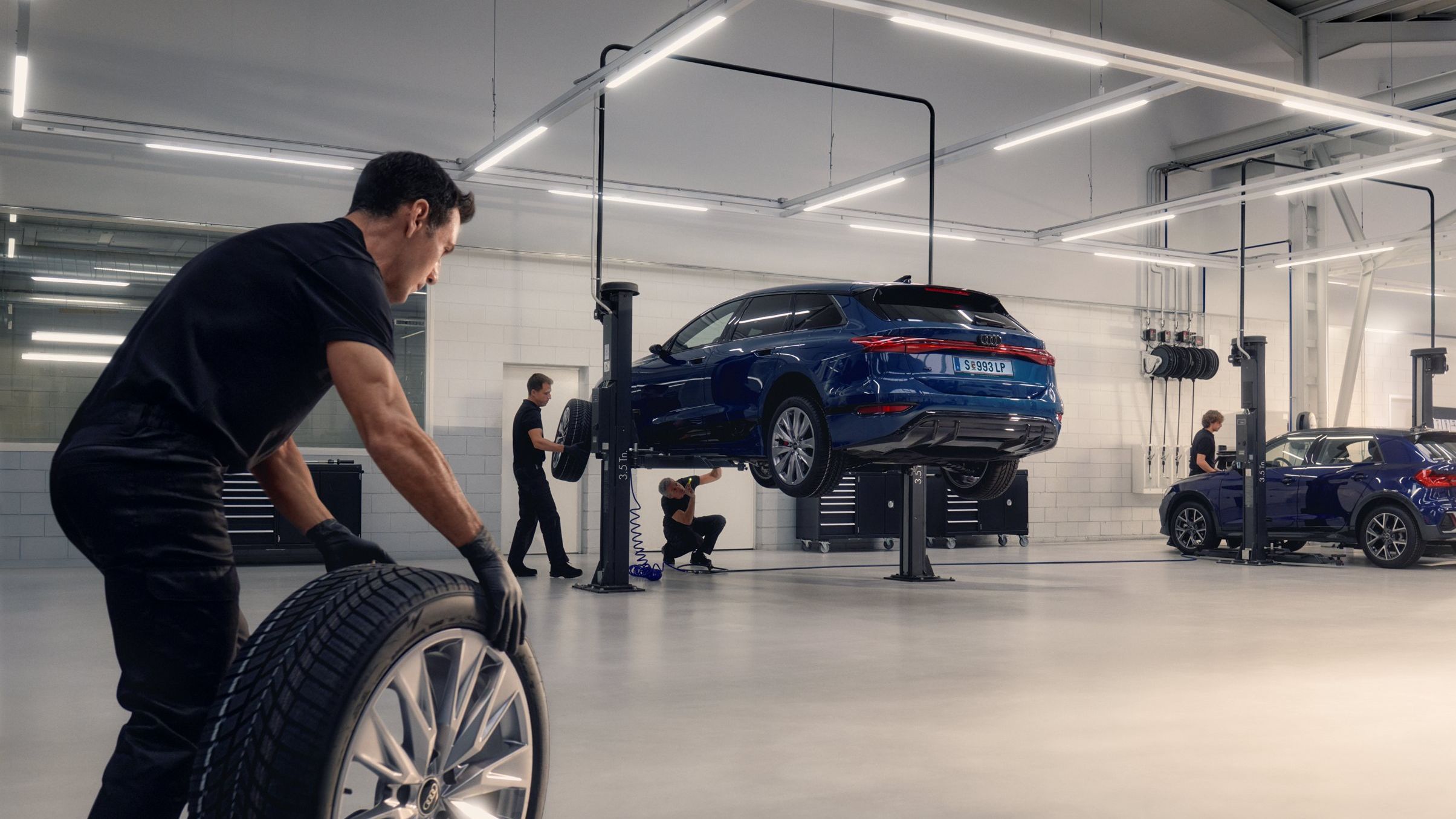 Ein Audi Mechaniker rollt ein Winterkomplettrad in Richtung eines Audi auf einer Hebebühne.