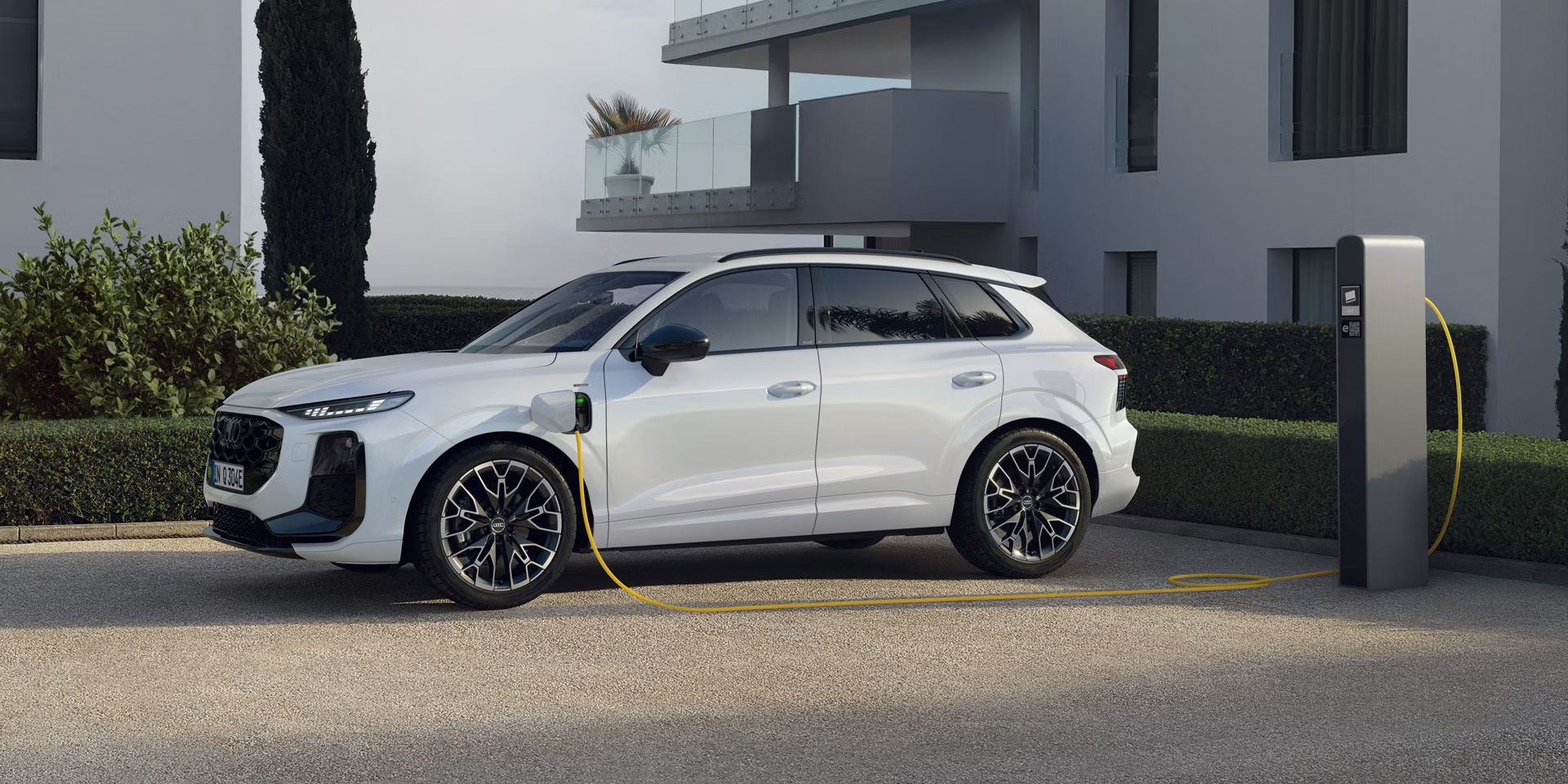 Weißer Audi Q3 SUV e-hybrid steht an der Ladesäule vor einem Gebäude