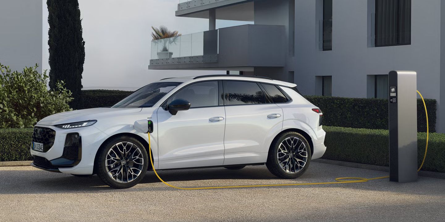 Weißer Audi Q3 SUV e-hybrid steht an der Ladesäule vor einem Gebäude