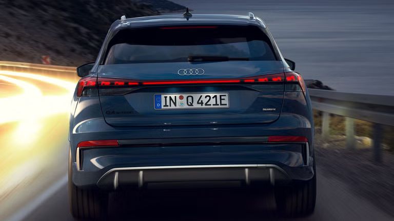 Der Q4 SUV e-tron von hinten bei Nacht auf einer abschüssigen Gebirgstraße, zur rechten das Meer. Auf der Gegenfahrbahn sind Lichtschleier entgegenkommender Fahrzeuge zu sehen. 
