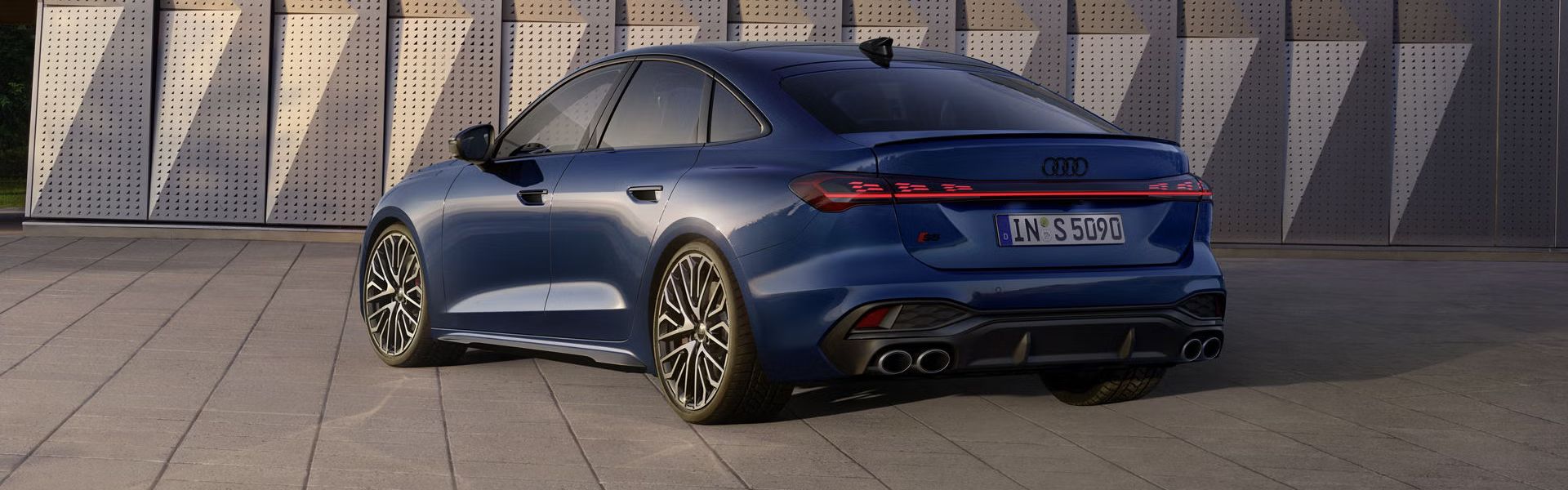 Die S5 Limousine in dunkelblau steht schräg vor einer Gebäudefassade und wird dabei vom Sonnenlicht angestrahlt.