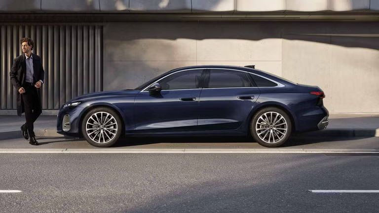 Die A6 Limousine im Seitenprofil in einer Parkbucht vor der Fassade eines Gebäudes. Vor dem Fahrzeug steht ein junger Mann.