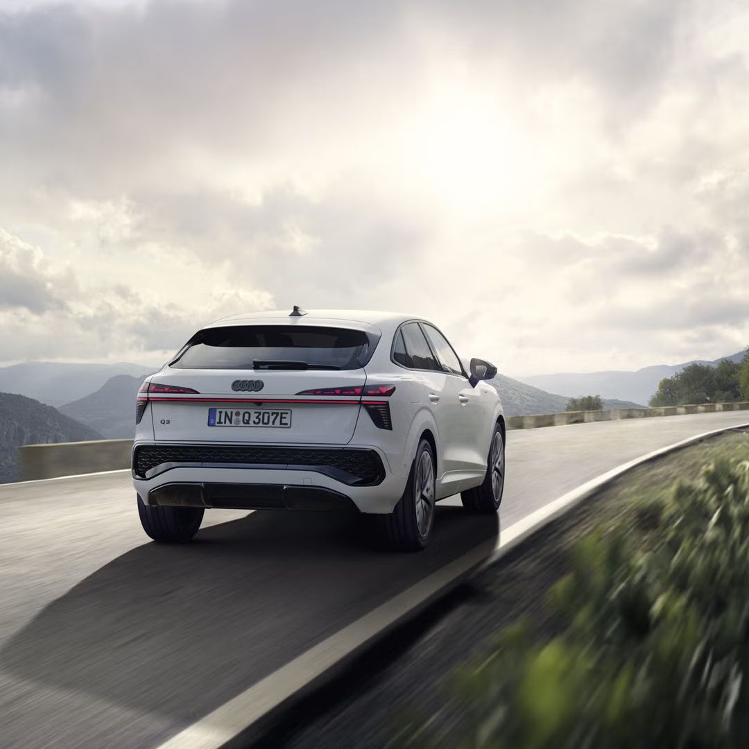 Ein weißer Q3 Sportback e-hybrid fährt auf einer Landstraße in einer bergigen Landschaft.	