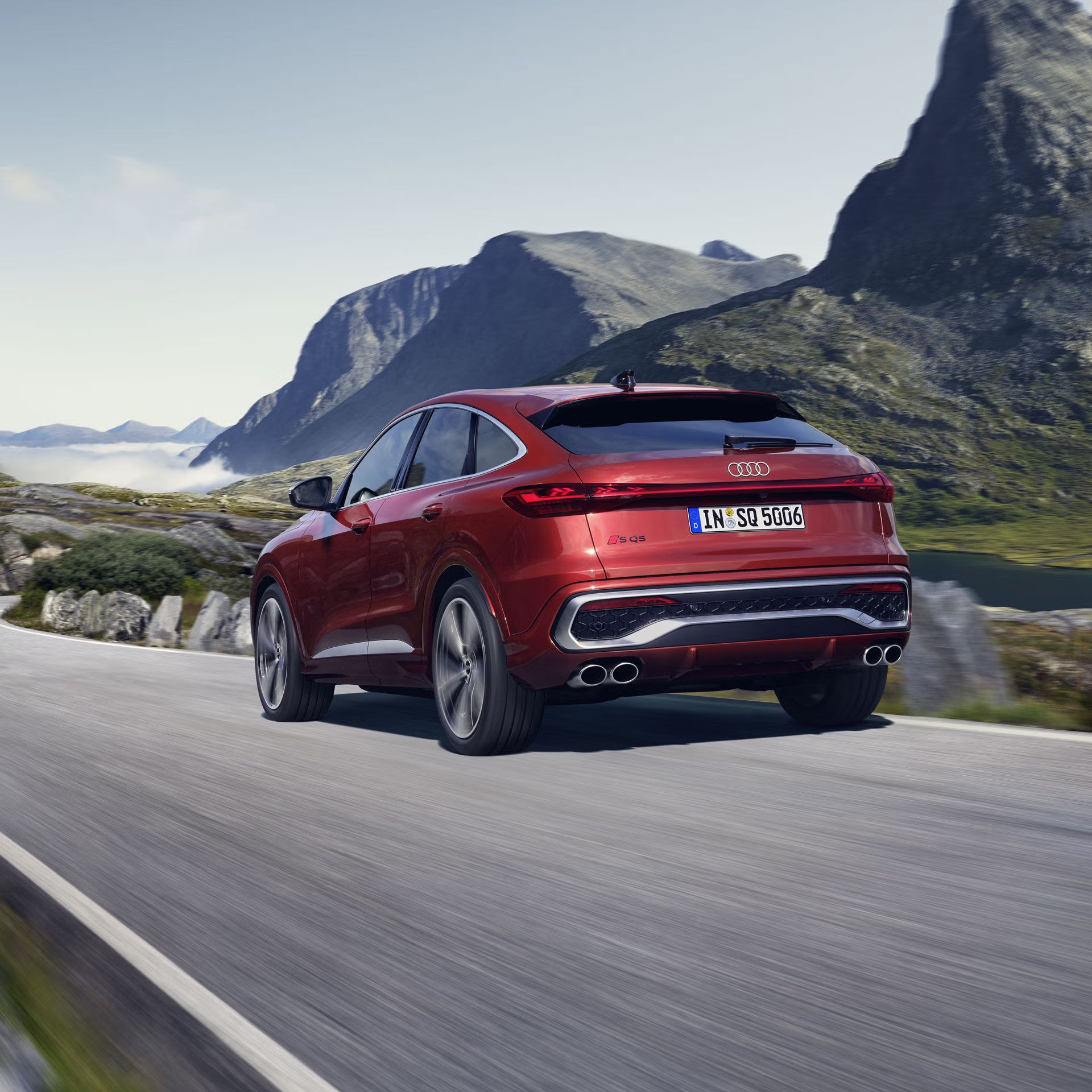 Schräges, hinteres Seitenprofil des roten SQ5 Sportback, welcher auf einer Straße durch die Berge fährt.