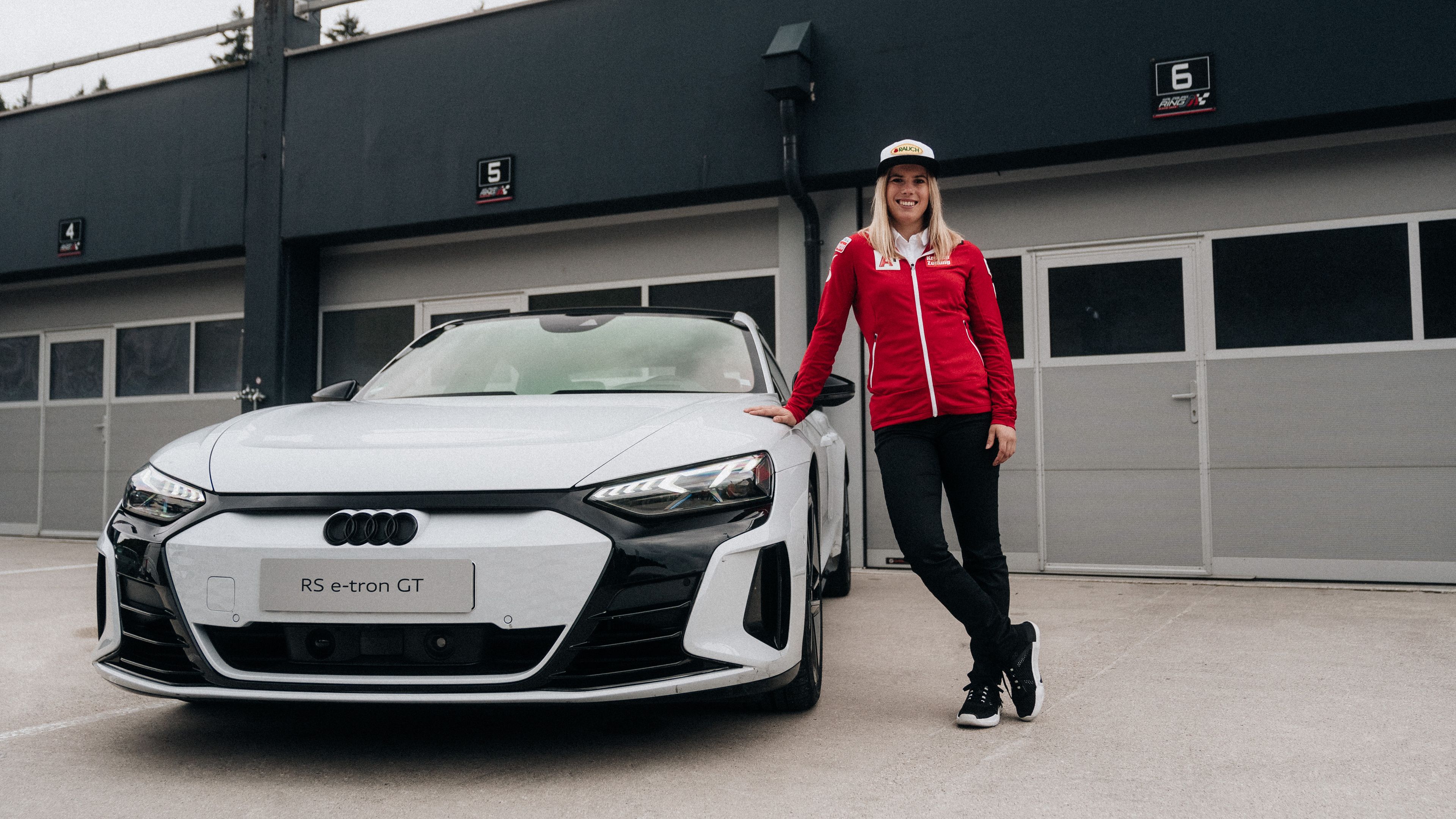 Skirennläuferin Katharina Liensberger lehnt an einem Audi RS e-tron GT vor einer Boxengasse.