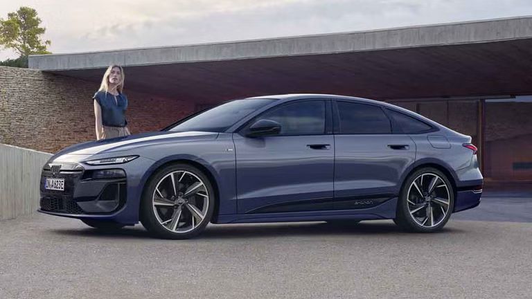 Der A6 Sportback e-tron steht im Seitenprofil vor dem Carport eines Hauses. Daneben steht eine junge Frau.