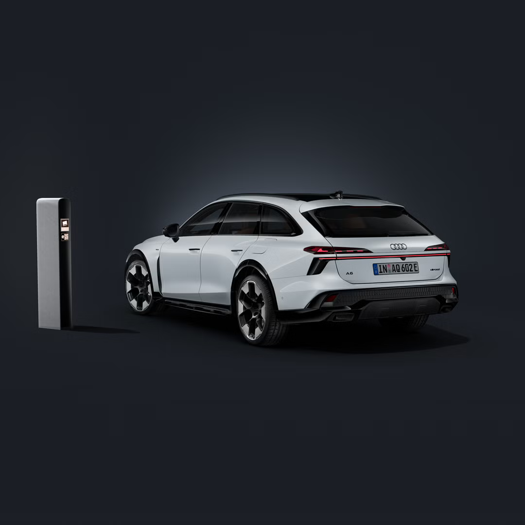 Der Audi A6 allroad e-hybrid schräg von hinten auf dunklem Hintergrund. Daneben eine moderne Ladesäule.