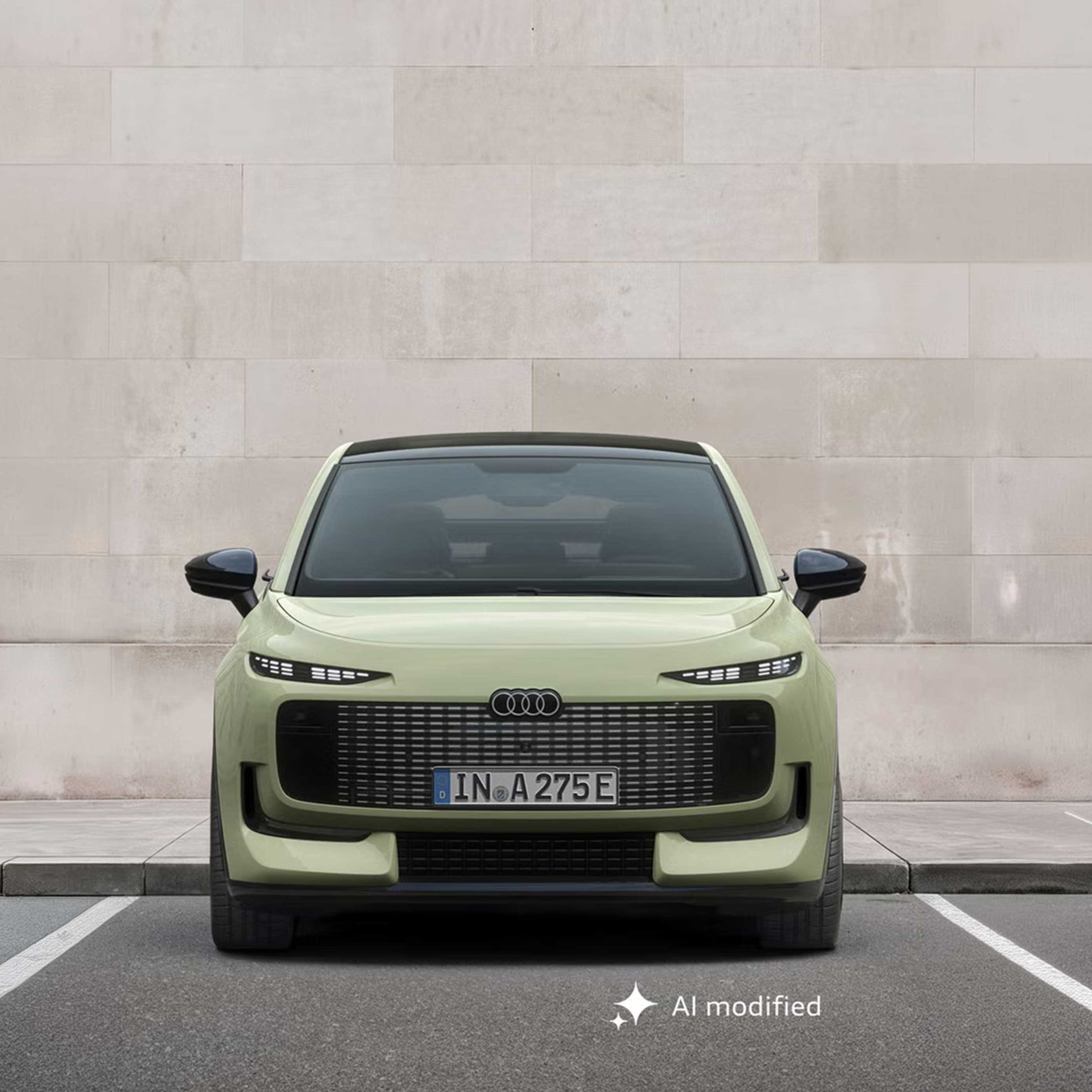 Der Audi A2 e-tron frontal von vorn auf einem Parkplatz, dahinter eine Gebäudewand in Steinoptik.