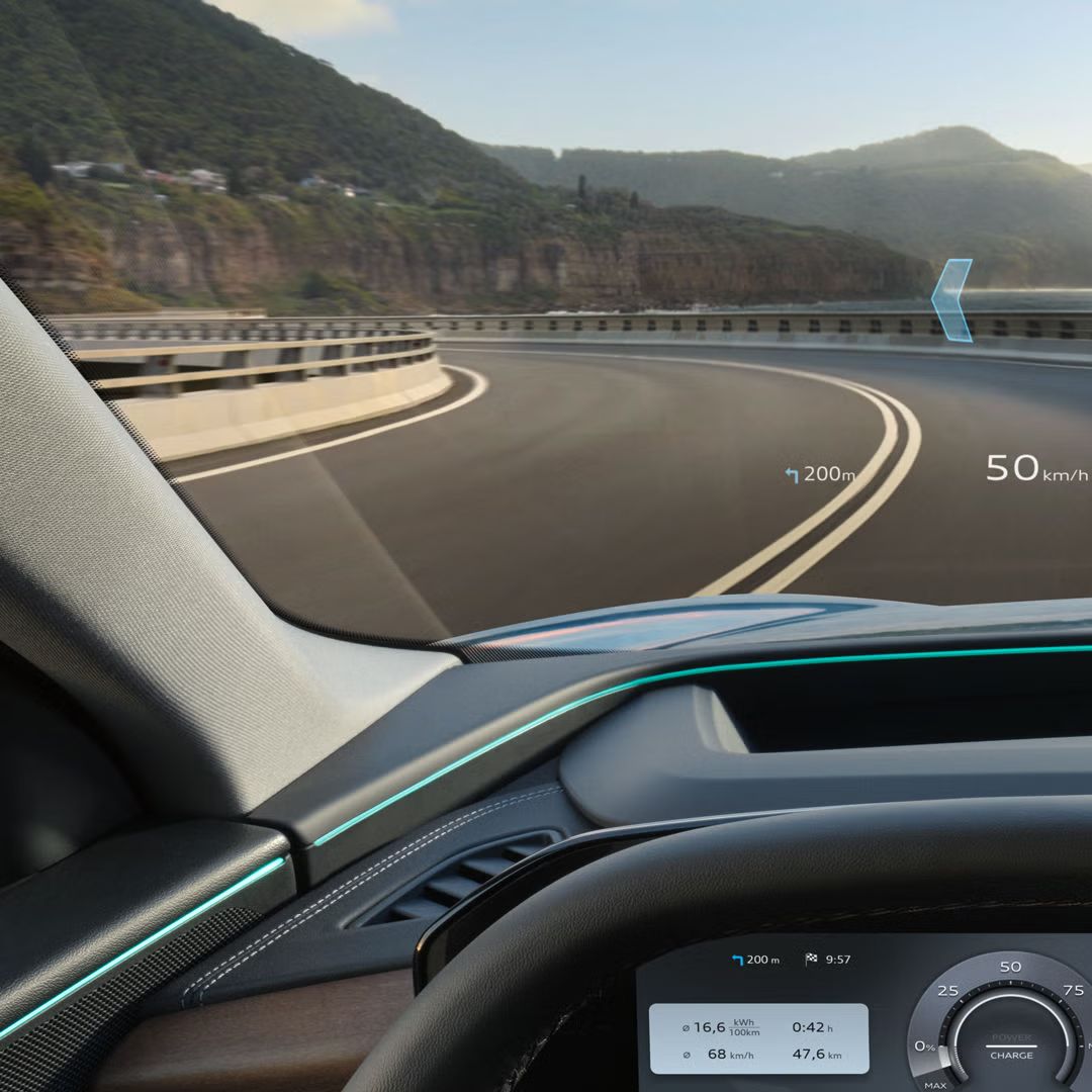 Der Q6 SUV e-tron aus Fahrerperspektive während der Fahrt. Das Head-up-Display zeigt Geschwindigkeit, Geschwindigkeitsbegrenzung, sowie die Navigation und den Verlauf der nächsten Kurve an.