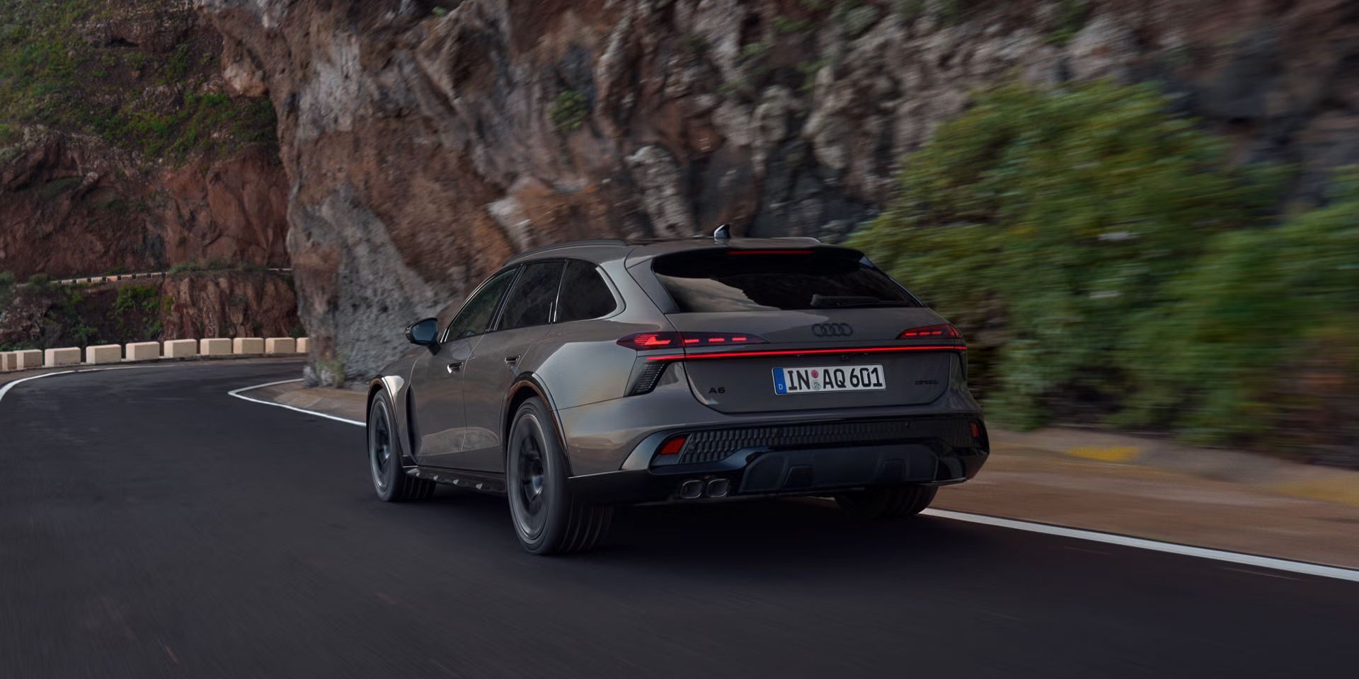 Der Audi A6 allroad schräg von hinten in voller Fahrt auf einer Gebirgsstraße. Rechts ragen steile Felswände auf.