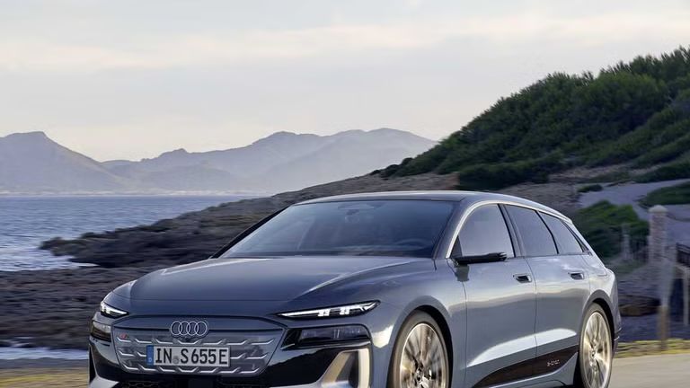 Der S6 Avant e-tron aus schräger Frontansicht, wie er eine Straße an der Küste entlangfährt. Im Hintergrund sind Berge zu sehen. 