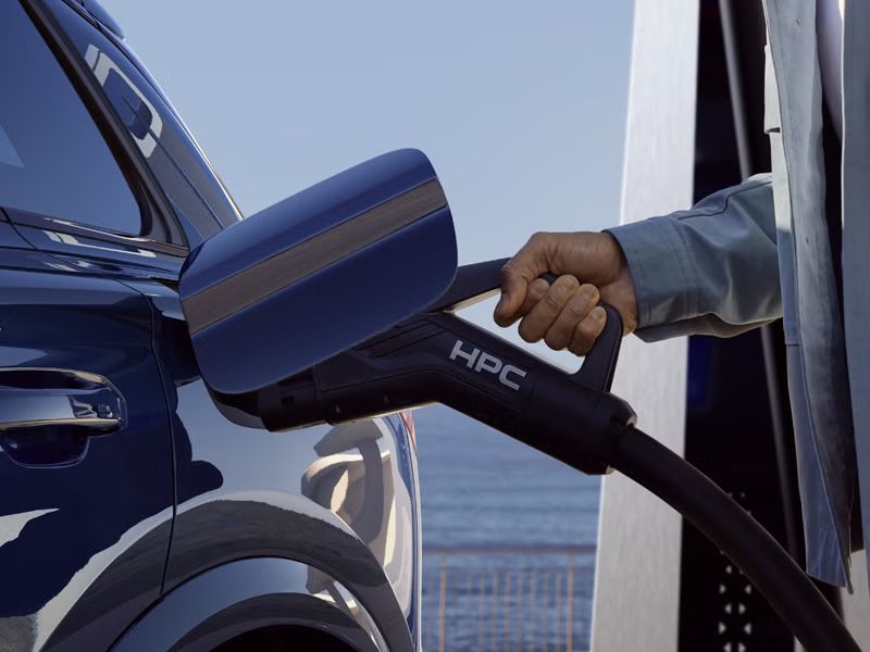 Eine Person steckt ein HPC-Ladekabel an einem Audi Fahrzeug an