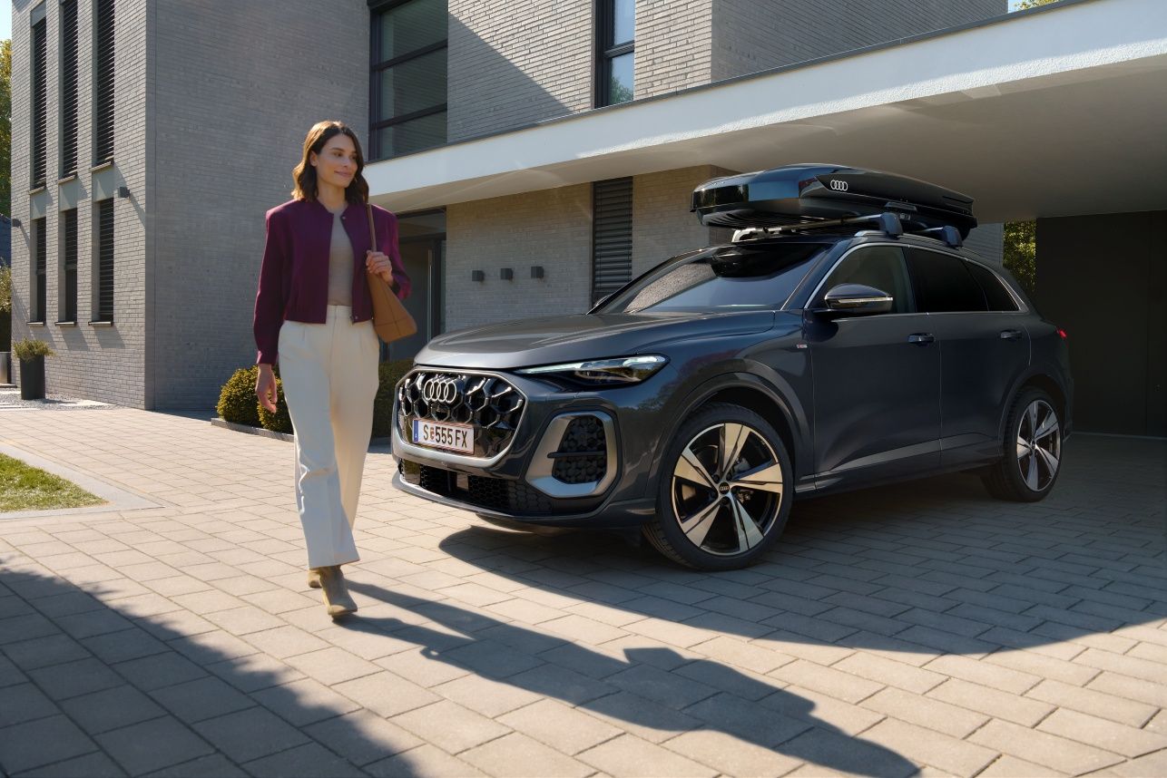 Frau passiert lächelnd einen in der Hauseinfahrt parkenden Audi Q5 mit Dachbox