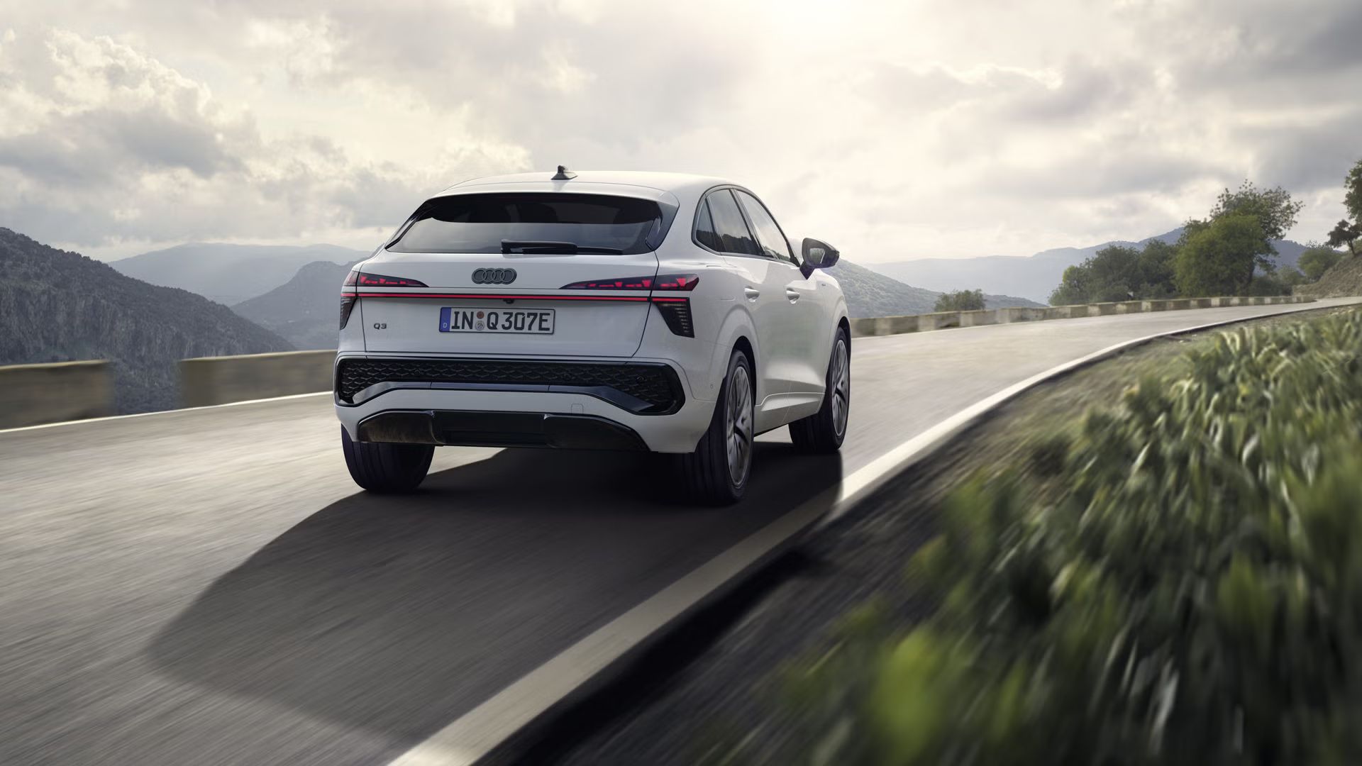 Ein weißer Q3 Sportback e-hybrid fährt auf einer Landstraße in einer bergigen Landschaft.	