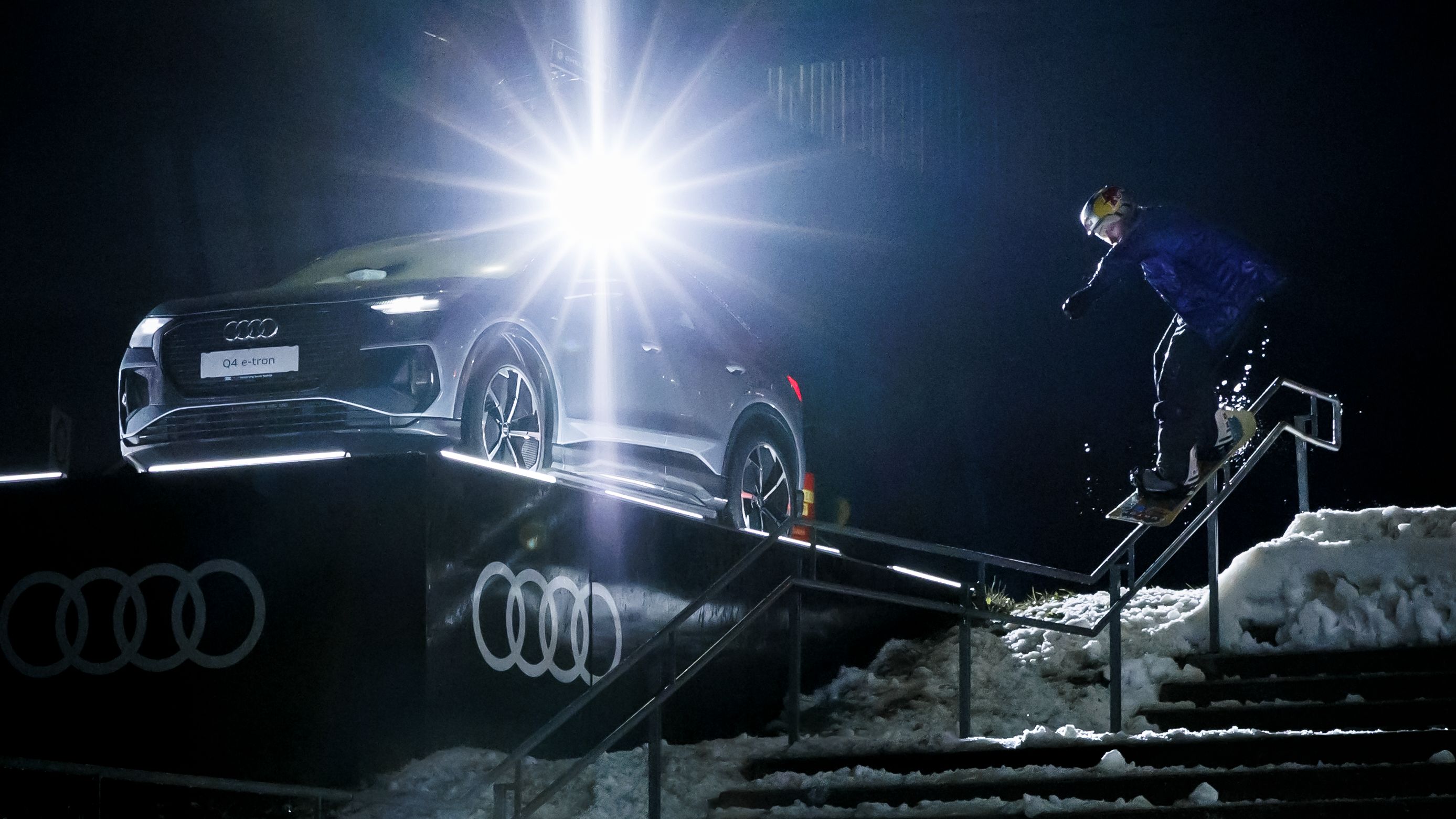 Clemens Millauer führt einen Rail-Slide direkt neben einem Audi Q4 e-tron aus, der auf einer erhöhten Plattform steht.