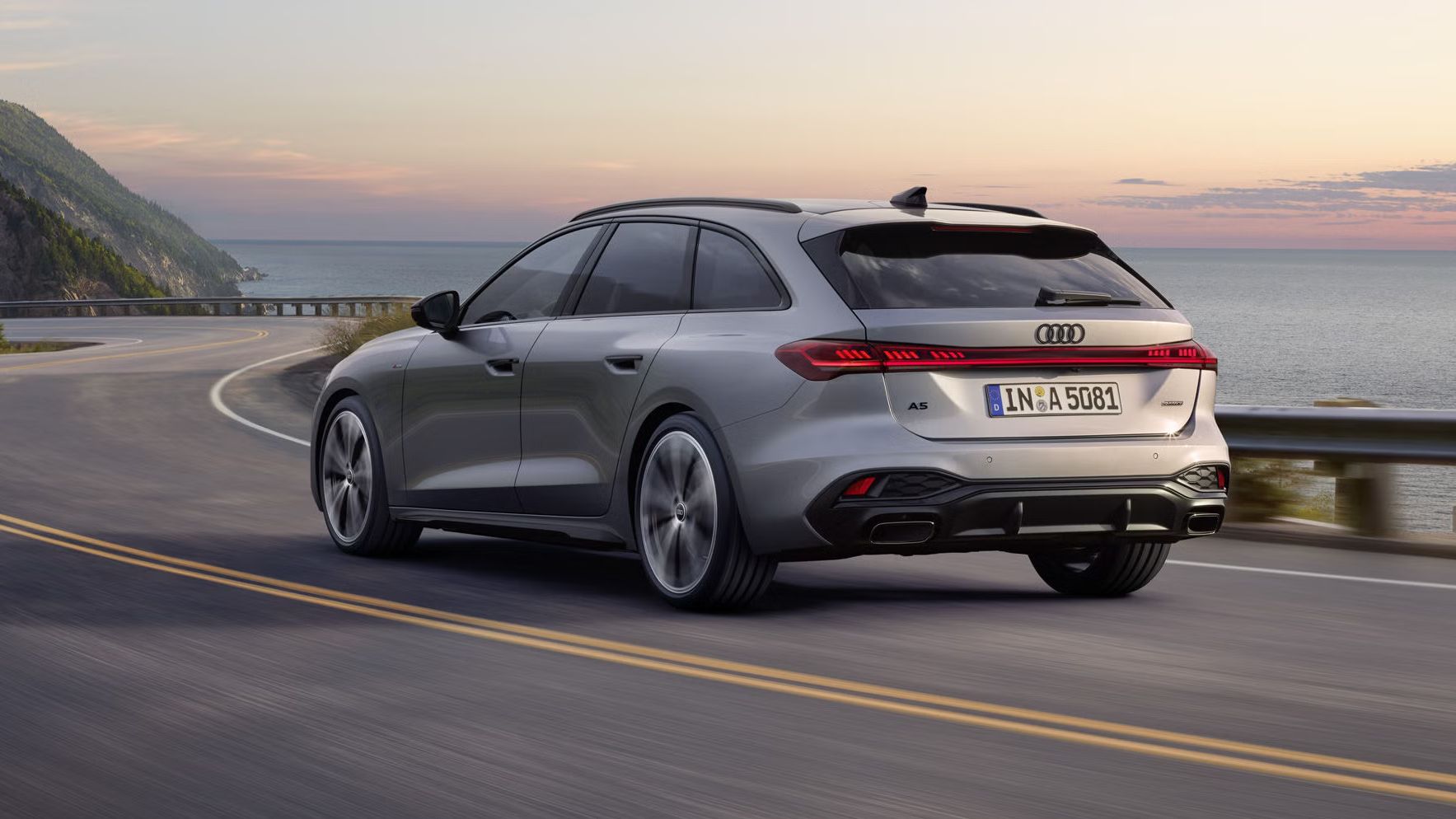 Der A5 Avant in einer schrägen Heckperspektive, während er bei Sonnenuntergang eine kurvige Küstenstraße entlangfährt.