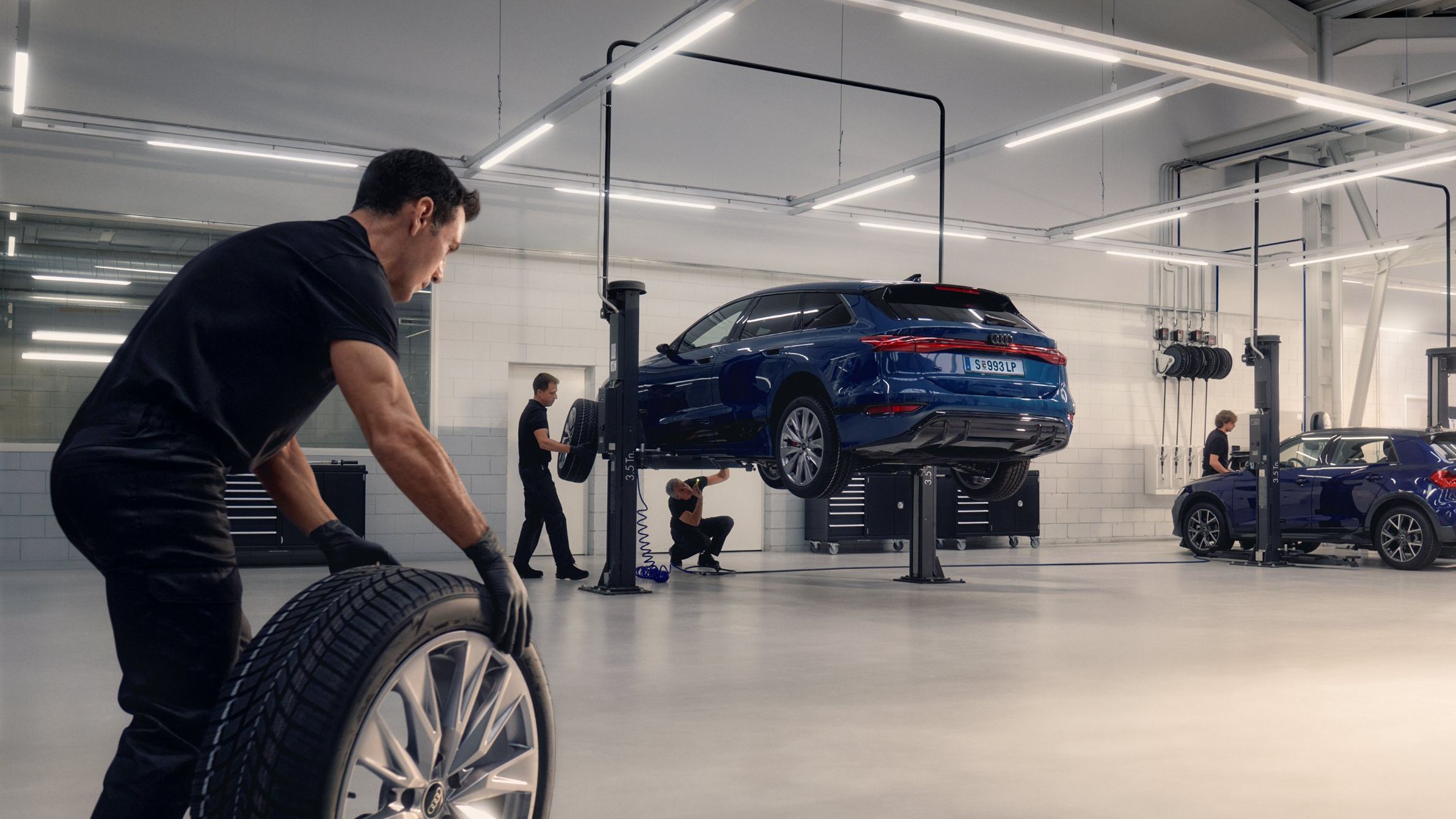 Ein Audi Mechaniker rollt ein Winterkomplettrad in Richtung eines Audi auf einer Hebebühne.