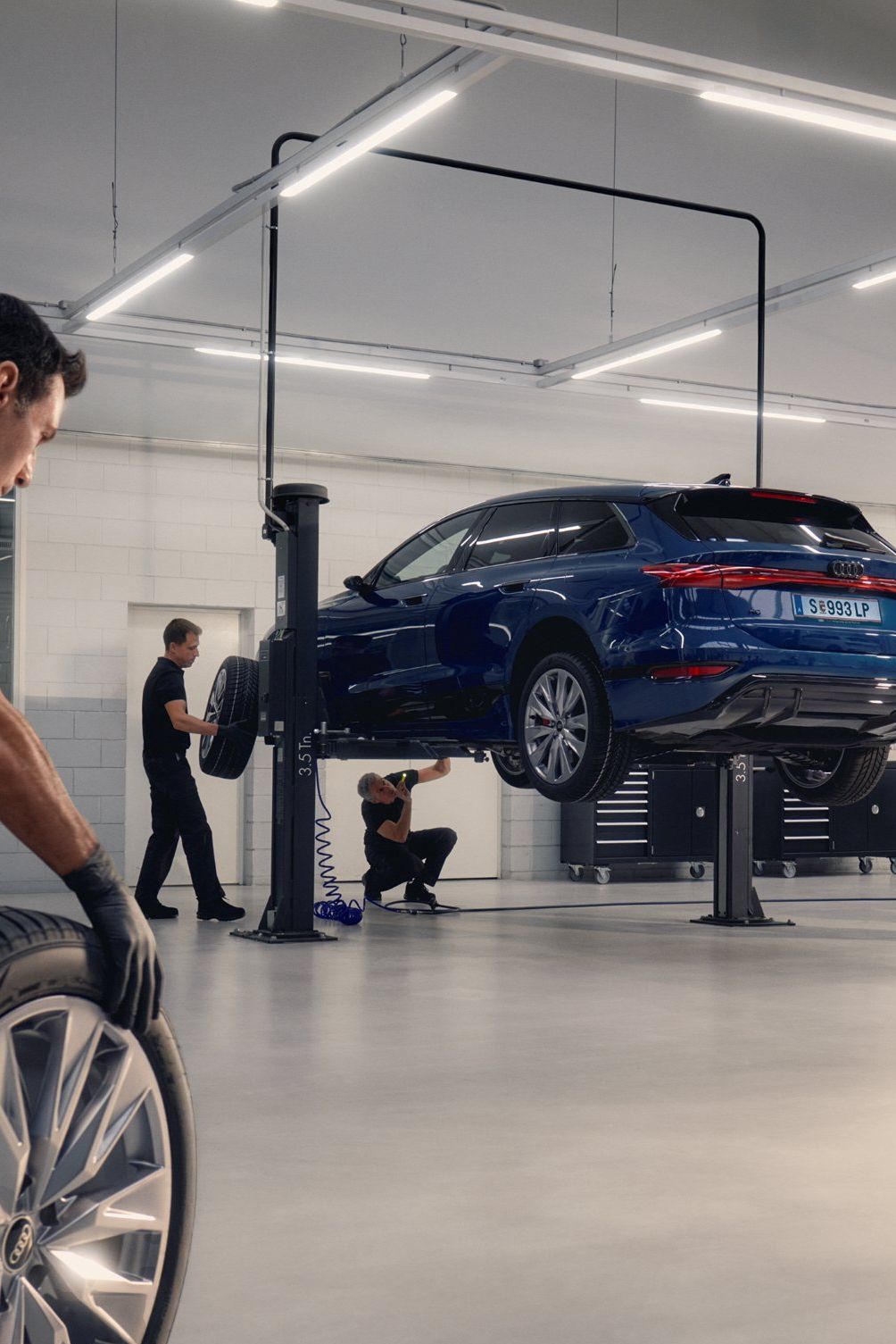 Ein Audi Mechaniker rollt ein Winterkomplettrad in Richtung eines Audi auf einer Hebebühne.