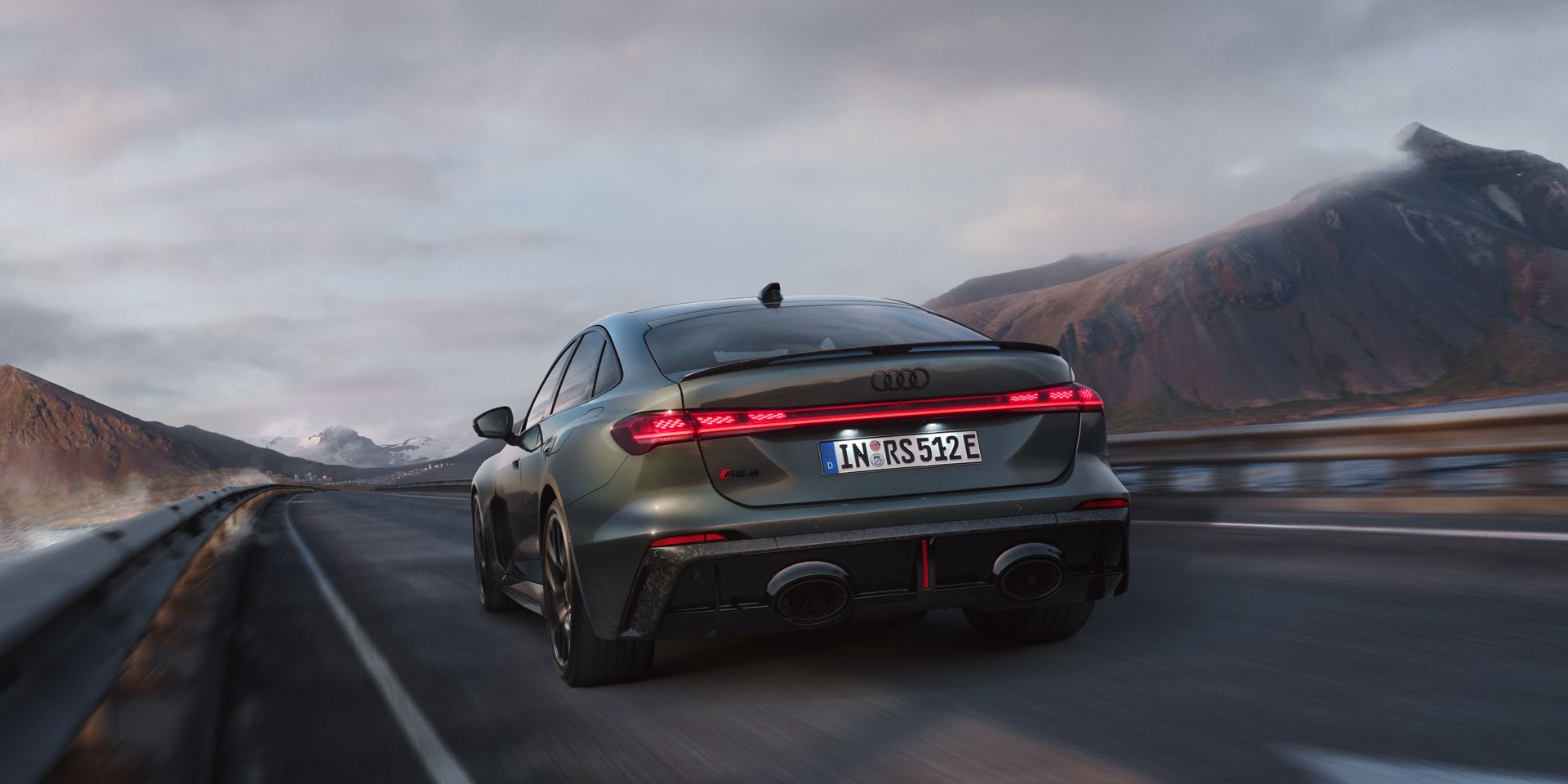 Die RS 5 Limousine fährt auf einer Gebirgsstraße. Rechts ein See, im Hintergrund schneebedeckte Berge. 